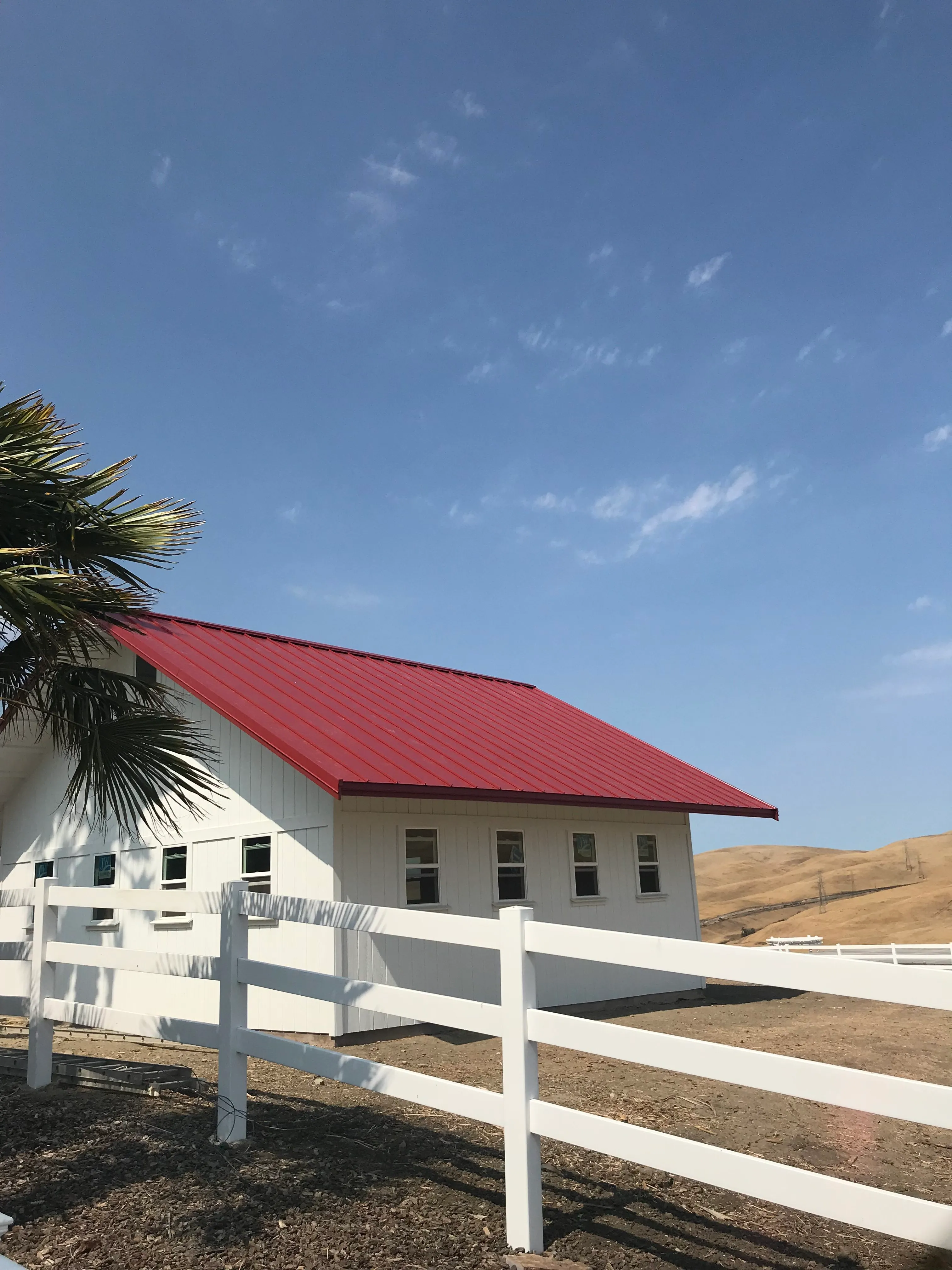 A white building with a bright red roof, surrounded by a white fence, set against a backdrop of clear skies and rolling hills in Livermore, California.